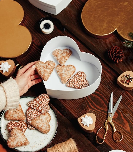 A person's hands carefully arranging homemade cookies in a decorative tin, with festive decorations and wrapping paper visible in the background.