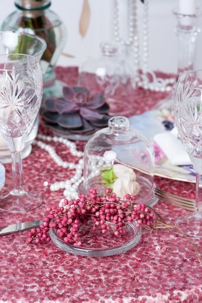 A table setting designed for a Hollywood glamour-themed party. The table is draped in a black sequined tablecloth and features star-shaped confetti sprinkled across the surface. There are tall vases holding lush white feather plumes and elegant candle holders with flickering candles.