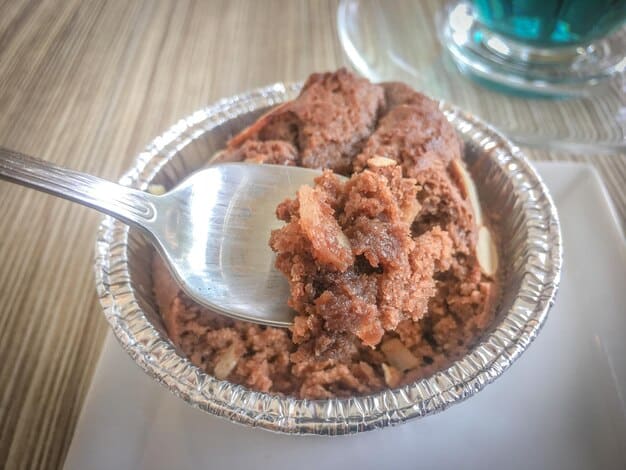 A close-up shot of a stainless steel bowl filled with colorful, homemade dog food, containing visible chunks of vegetables and meat. A measuring cup sits beside the bowl.