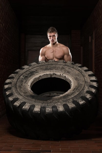 A person skillfully repurposing an old tire into a weightlifting tool in their garage gym. The tire is painted and fitted with handles, showcasing a creative and budget-friendly approach to home fitness.