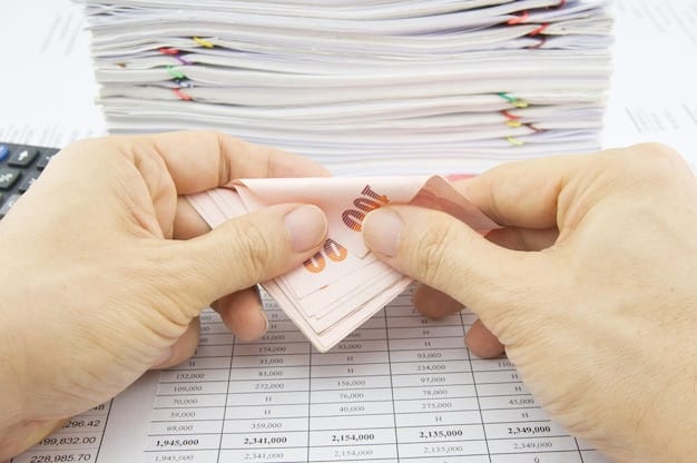A person's hands are busy organizing neatly stacked bills into several labeled envelopes on a wooden table, with one envelope prominently labeled 